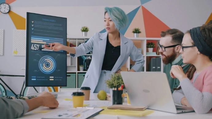 A woman with blue hair pointing at a digital chart during a team meeting